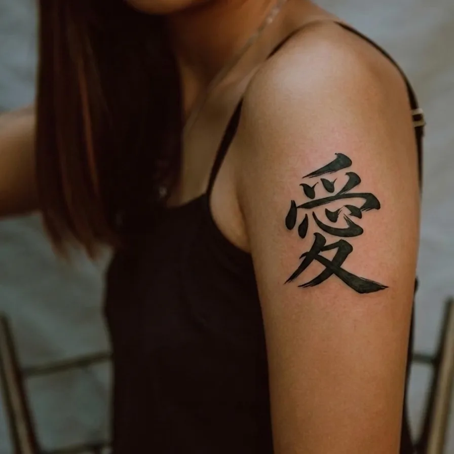 愛 (Ai) — kanji for love, brush calligraphy tattoo on arm